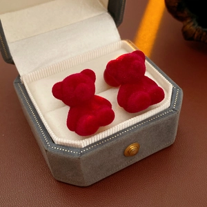 Macro shot of red flocked bear stud earrings placed inside a grey hexagonal jewelry box