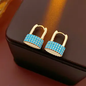 Minimalist gold lock earrings with inlaid blue stones on dark leather background