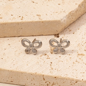 Close-up of silver butterfly stud earrings on a textured beige stone background