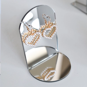 Golden heart earrings with white faux pearls on a mirrored jewelry display stand