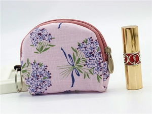 Floral fabric coin purse with gold zipper and keychain next to a lipstick prop