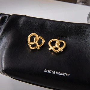 Close-up of gold heart-shaped stud earrings on a black textured leather background