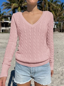 Detail of pink cable knit V-neck sweater with ribbed cuffs on a model at the beach