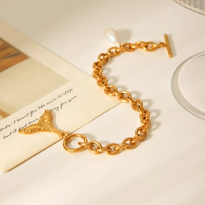 Detail eines Goldkettenarmbands mit Fischschwanz-Anhänger und weißer Perle auf einer Karte