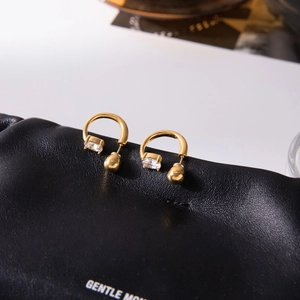 Detailed macro view of 18K gold C-shaped earrings with oval zircon and polished beads