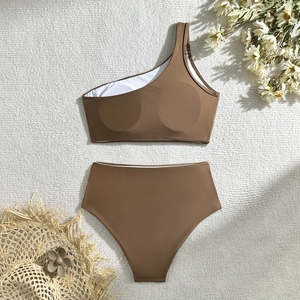 Flat lay of deep brown one-shoulder bikini top and high-waisted bottoms on a white blanket
