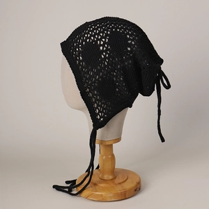 Détail d'un bonnet au crochet noir ajouré avec lacets sur un mannequin en bois