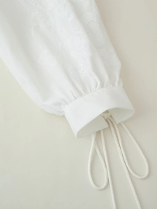 Detail of white embroidered cotton-linen sleeve with drawstring and tassel fringe