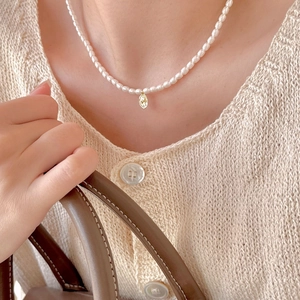 Close-up of pearl necklace with a gold oval embossed pendant worn on a beige knit sweater