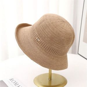 Khaki knitted bucket hat for women with elegant golden metal badge on a display stand