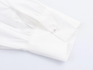 Close-up of elegant pleated cuff with a round pearl button on a white cotton blouse