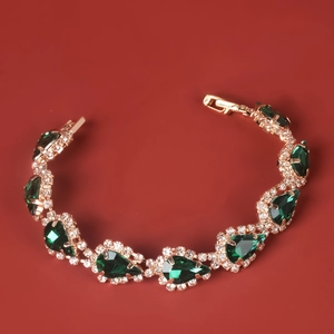 Bracelet doré élégant avec cristaux verts en goutte et zircons sur un fond rouge foncé chic