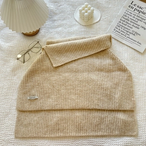 Detail of beige knit turtleneck poncho vest with ILLDI PLAN label in a cozy setting