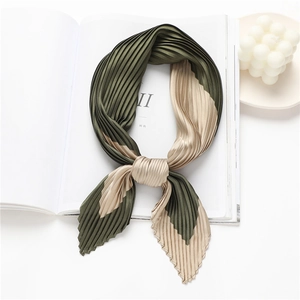 Pleated silk scarf in dark green and champagne gold on a minimalist white backdrop