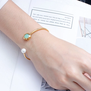 Detailed view of an open gold bangle with green flower stone and white pearl detail