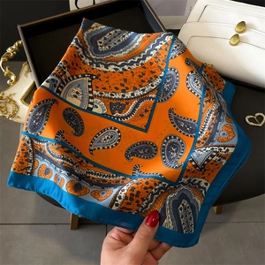 Detail of orange and blue paisley silk scarf draped over a white luxury handbag