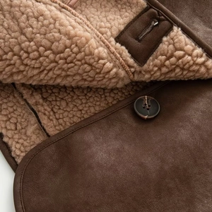 Detail of dark brown leather jacket with beige faux shearling lining and resin button