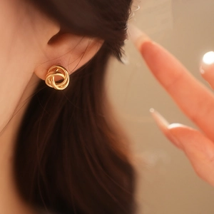 Gros plan de boucles d'oreilles nœud torsadé doré portées par un mannequin en douceur