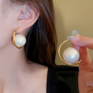 Detailed close-up of a golden circular earring featuring an elegant white pearl center