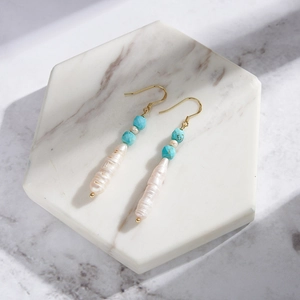 Detail of bohemian drop earrings with natural pearls and turquoise on marble base
