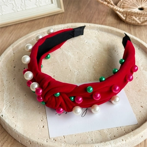 Détail d'un serre-tête noué rouge orné de perles blanches, vertes et roses sur plateau