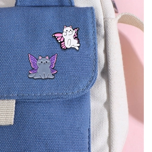 Broches chat en émail avec ailes de papillon épinglées sur un sac en toile bleue
