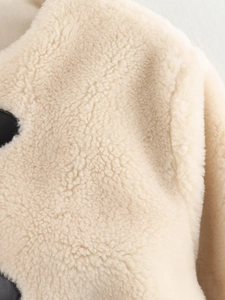 Close-up of cream fleece fabric texture with black faux leather trim on a jacket