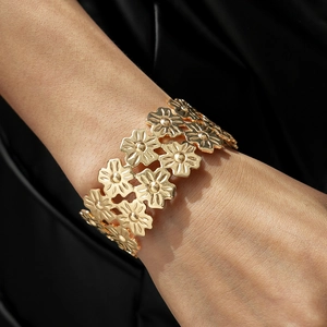 Detailed view of a layered gold flower bangle with hollow floral patterns on dark fabric
