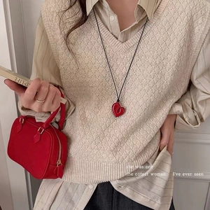 Red heart pendant necklace with black cord cord styled with a beige knit vest and bag