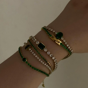 Close-up of layered gold bracelets with green emerald-cut stones and white zircon accents