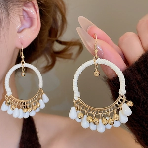 Detail showing bohemian woven cotton rope earrings with gold pendants and white resin beads