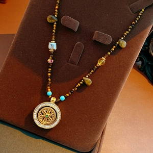 Detail of tiger eye bead necklace featuring a golden mandala pendant with white crystals