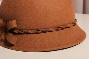 Detail of caramel wool cloche hat with mink fur pompom and rhinestone bow decoration