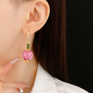Nahaufnahme von Blumen-Glaskugel-Ohrringen mit Goldhaken an einem Model vor schwarzem Grund