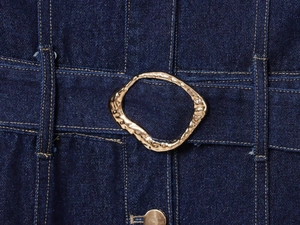 Detail of a golden hammered metal belt buckle on a dark blue denim dress fabric