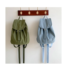 Dettaglio di zaini in nylon verde oliva e blu chiaro appesi a un rack di legno