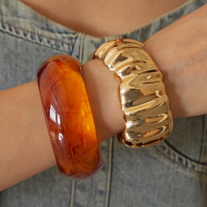 Detail of amber translucent resin and gold textured metal thick bangle bracelets