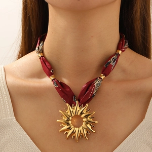 Detail of a large sunburst gold pendant with a vintage burgundy printed silk ribbon strap