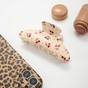 Acetate hair claw clip with red cherry pattern and rhinestones on a white background