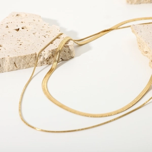 Detail of layered gold snake bone chains draped over textured stone with soft lighting