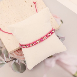 Pink bohemian woven bracelet with purple beads and silver charms on a jewelry pillow
