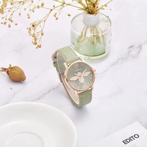 Detail of rose gold watch featuring a gold bee motif on a sage green textured dial