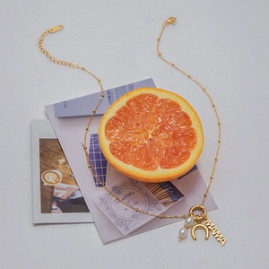 Macro detail of gold-plated titanium necklace with MAMA pendant and pearls on orange