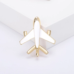 Minimalist gold metal airplane brooch with white enamel detail on white podium