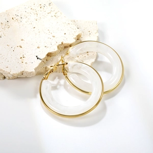 Minimalist round gold earrings with marble white resin on beige stone prop