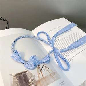 Close-up of blue woven headband with white flowers, bow detail and ribbons on a book