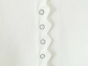 Detail aus weißem Strickstoff mit silbernem Metalldruckknopf und gewelltem Muschelsaum