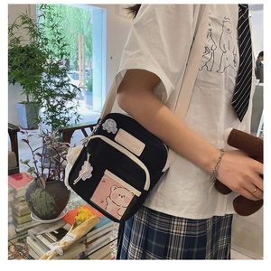 Détail de la besace noire en toile avec écusson ours et poche transparente