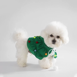 Detail view of a green pet Christmas cape with colorful pom-poms on a white dog