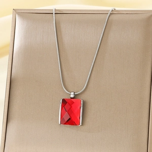 Detailed shot of red rectangular crystal pendant on silver snake chain over golden box